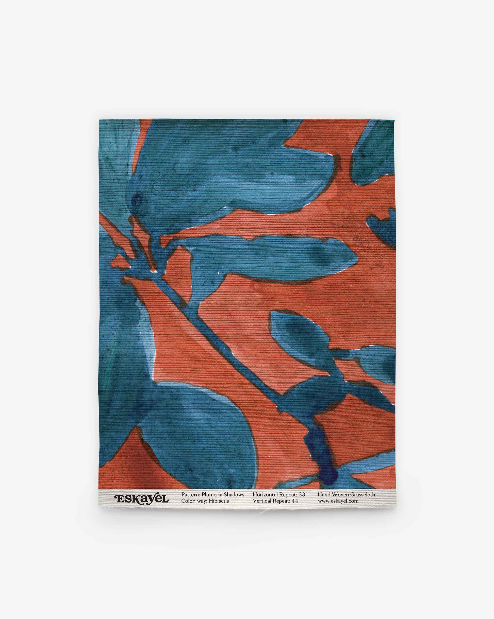 A swatch of Eskayel’s Plumeria Shadows grasscloth wallpaper pattern in Hibiscus, a colorway with a rich red background.