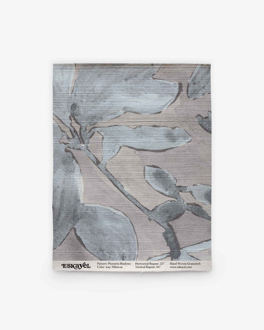 A sample swatch of Plumeria Shadows Grasscloth Sample||Shadow, showcasing a subtle blue and gray abstract leaf design, complete with product and brand details along the bottom. Ideal for discovering new design possibilities—Order a sample today to experience this fabric in person.