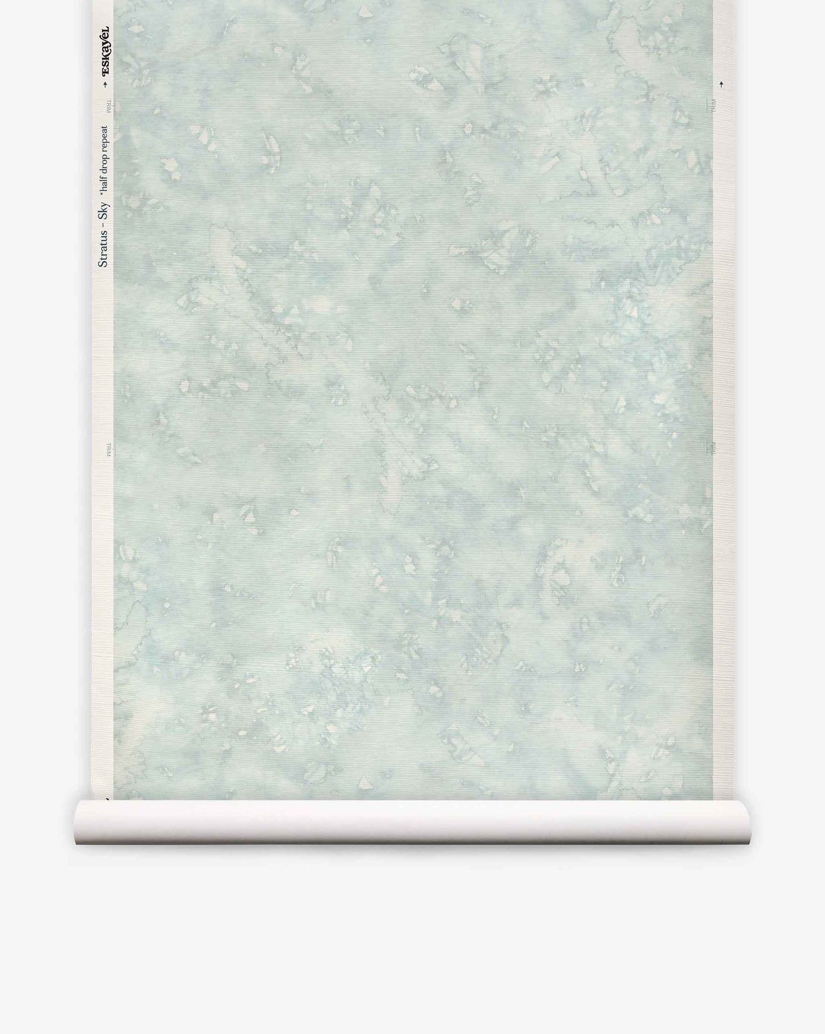 A partially unrolled roll of Stratus Grasscloth||Sky wallpaper, featuring a pale blue marbled design with subtle white and gray accents, is displayed against a white background.