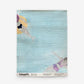 Swim Grasscloth||Sea light blue coastal wallpaper featuring a watercolor pattern of two swimmers floating in water.