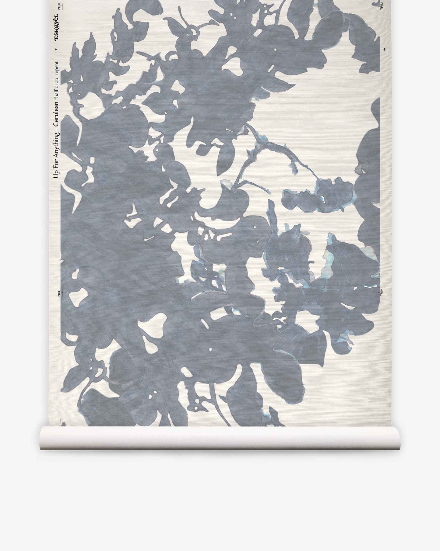 The Up for Anything Grasscloth||Cerulean wallpaper roll features a large, abstract blue-gray floral pattern on a light background, unrolled and displayed vertically to showcase its sophisticated watercolor effect and abstract botanical design.