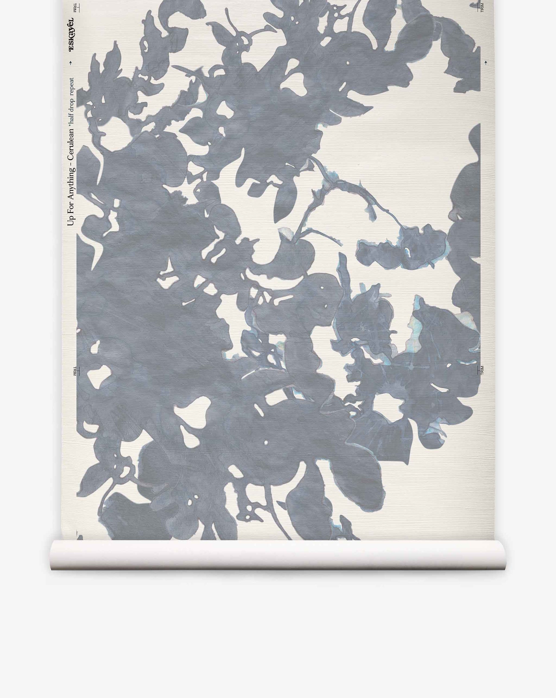 The Up for Anything Grasscloth||Cerulean wallpaper roll features a large, abstract blue-gray floral pattern on a light background, unrolled and displayed vertically to showcase its sophisticated watercolor effect and abstract botanical design.