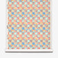A roll of Yaya Grasscloth||Punch coastal aquarelle wallpaper featuring a checkered pattern of abstract shapes in shades of pink, orange, and blue.