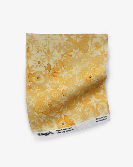 A fabric swatch in Eskayel’s Crochet Lace micro-print design in Limoncello displays yellow and gold tones.