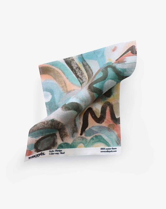 A twisted scarf in Floripa Fabric Sample||Reef with a colorful abstract pattern and a label displaying "100% Egyptian linen" and a designer signature.