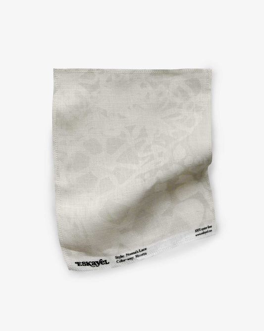 A fabric swatch of Nonna’s Lace in Ricotta shows a closeup of the design in a palette of beige and neutral.