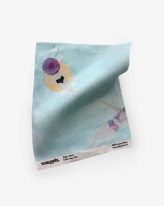 A light blue microfiber cloth with a minimalist design featuring a painted figure. Branding and text "Esquivel, Sofie Satin Cotton, Sugar Sea" are printed at the bottom edge. Request a **Swim Fabric Sample||Sea** to experience its quality before placing an order.
