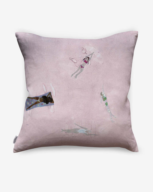 The Swim Pillow in Shell has a pale pink background, showcasing four illustrated swimmers in different poses for a beach house feel and elegant watercolor style on the front.