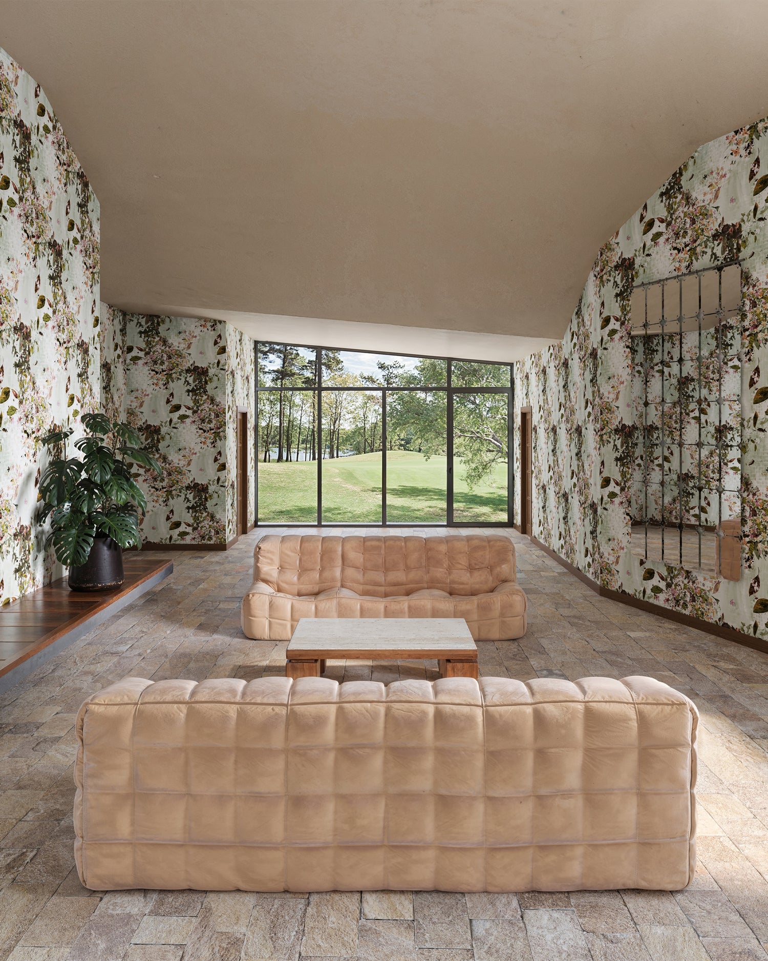 Modern living room with beige sofas and a large window overlooking lush greenery with Eskayel's Petalos wallpaper in Abalone on the walls. 