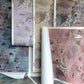 Sheets of Custom Silk Wallcovering samples with underwater-themed patterns in muted shades—blue, purple, brown, and pink—are displayed overlapping each other.
