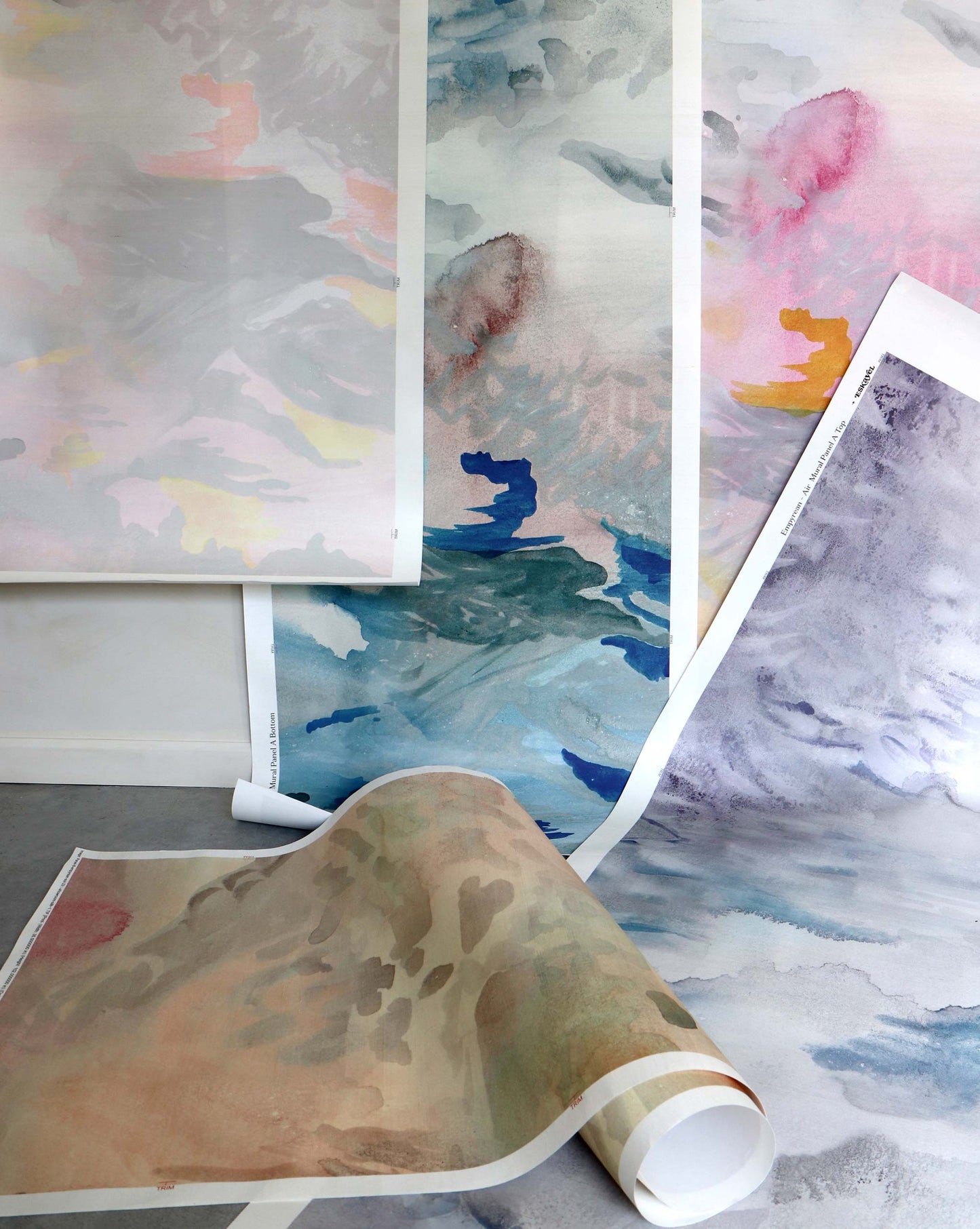 Custom Silk Wallcovering is showcased with large sheets featuring abstract watercolor designs in muted tones, displayed both upright and rolled on the floor, inspiring unique and personalized silk patterns.