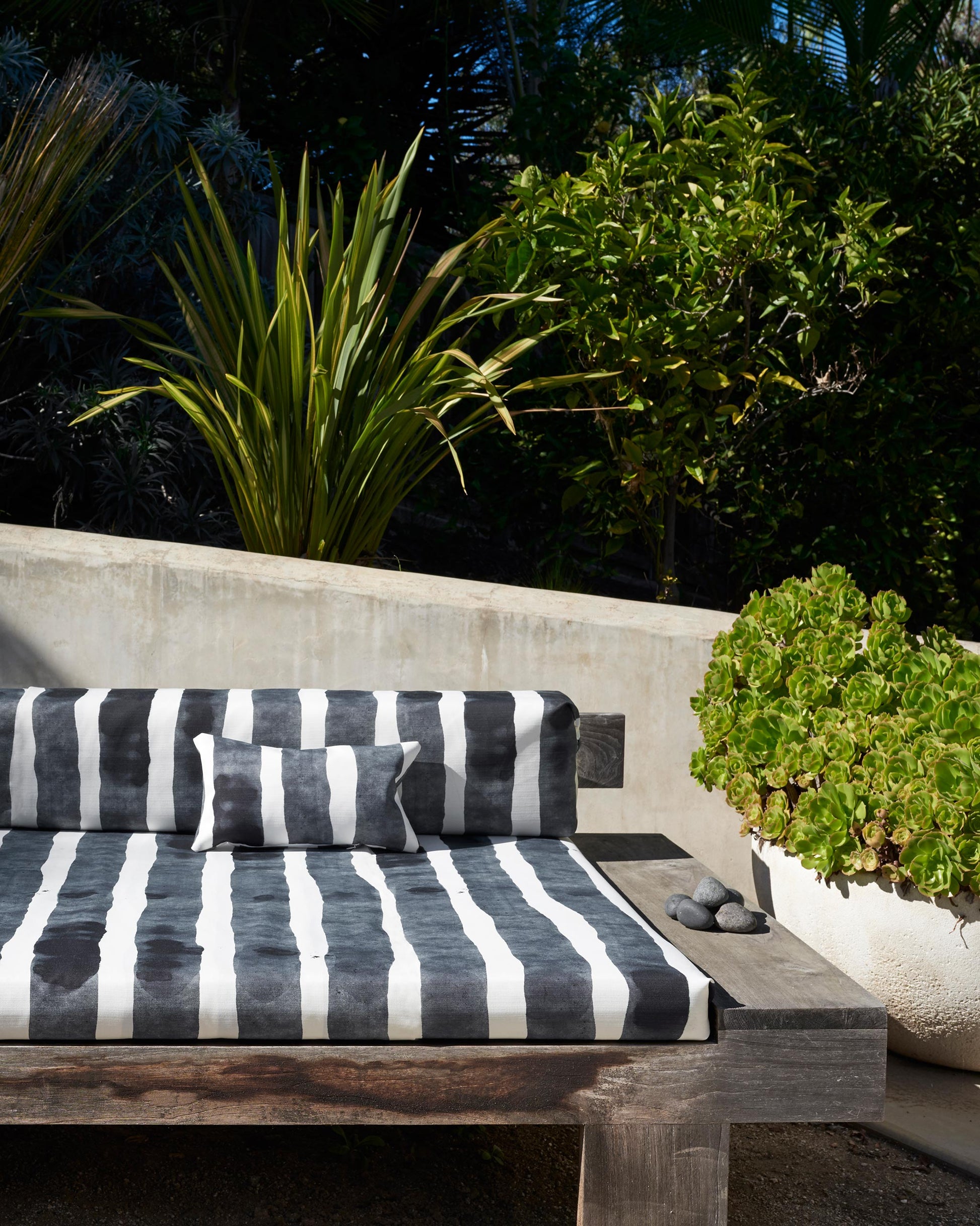 A black and white striped Bold Stripe Performance Fabric Slate cushion from the Eskayel Stripes Collection, made of luxury performance fabric, on a wooden bench