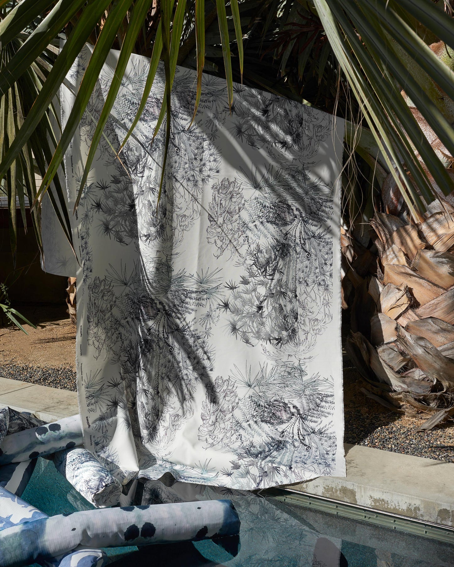 A luxury performance fabric with the Domenica Performance Fabric Notte pattern, featuring a palm tree design, placed next to a pool in the Salentu Collection