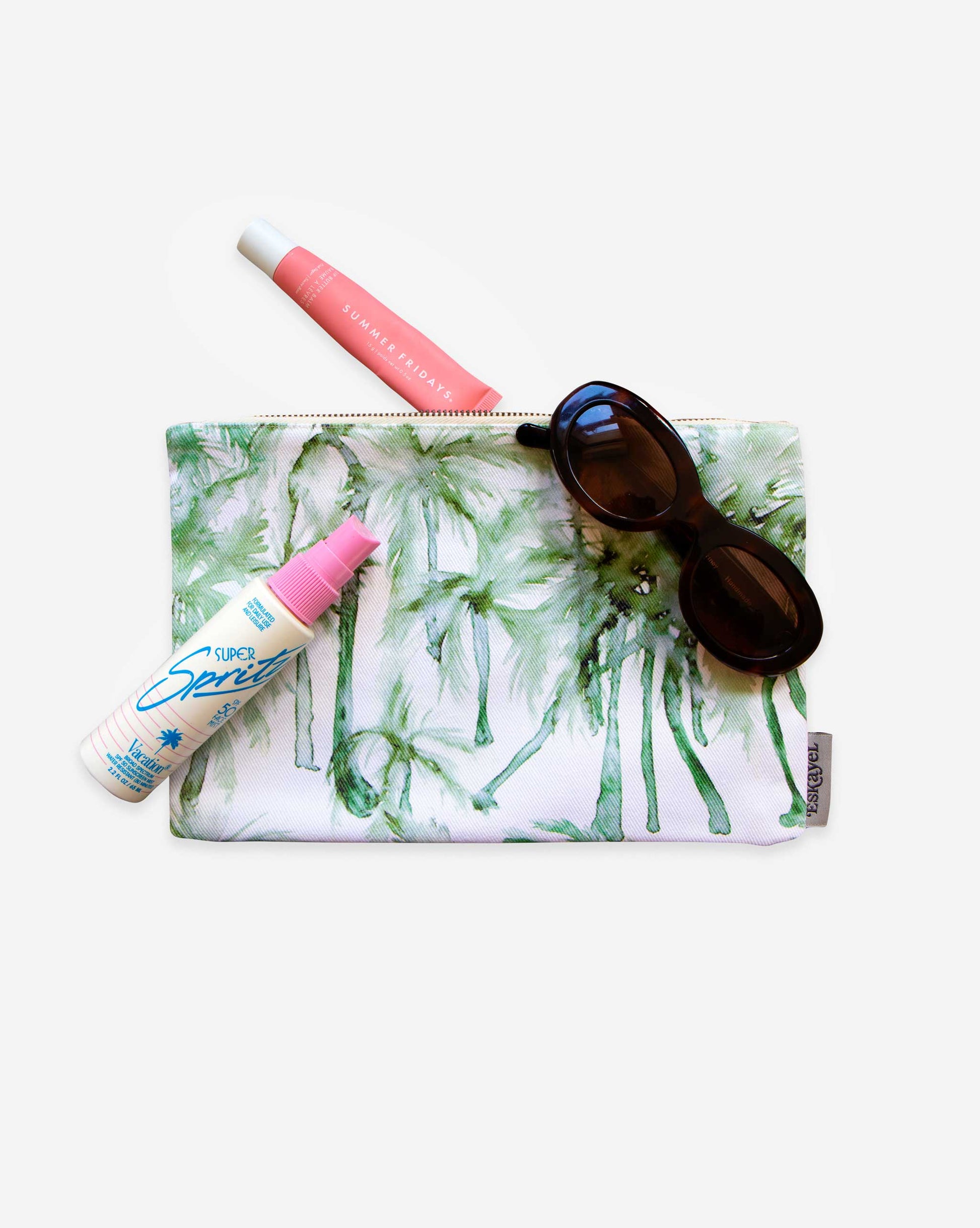 The Chloros Palm Dance Pouch brings a tropical vibe, with chic sunglasses, pink lip products, and sunscreen spray neatly arranged on a white background. It's perfect for storing all your vacation essentials in style.