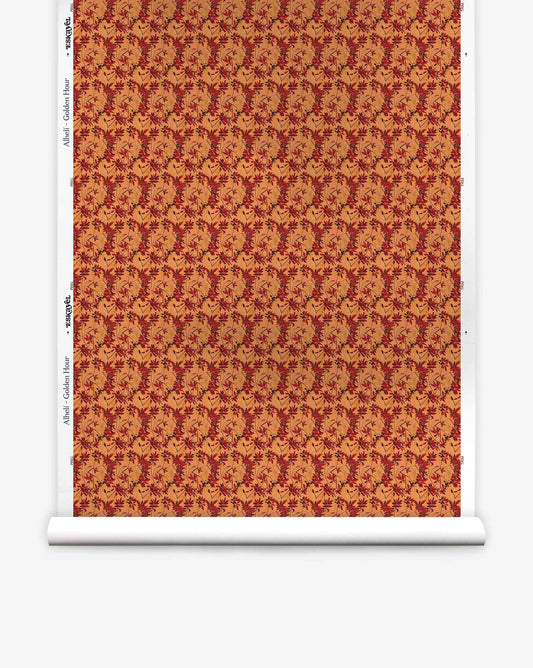 A roll of Alhelí Silk Wallcovering in Golden Hour, featuring a repeating pattern of dark red autumn leaves on a warm, golden-orange background.