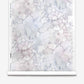 A roll of Aquarelle Silk Wallcovering in Ice, featuring a pale, marbled watercolor pattern in shades of grey, blue, and violet.