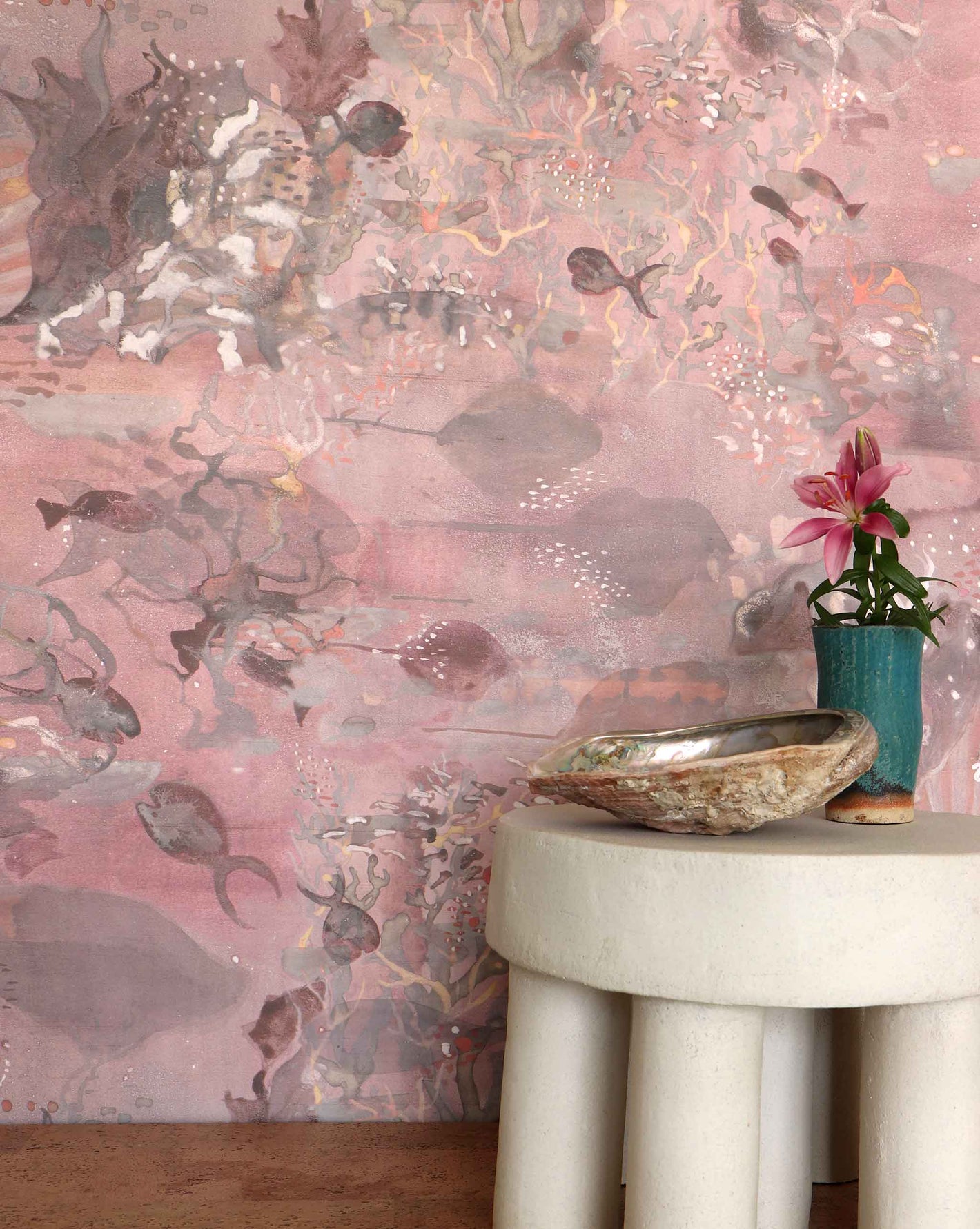 Eskayel’s Atoll wallpaper in Coral with its red hues is printed on a paper backed silk and installed in a room behind a stone stool.