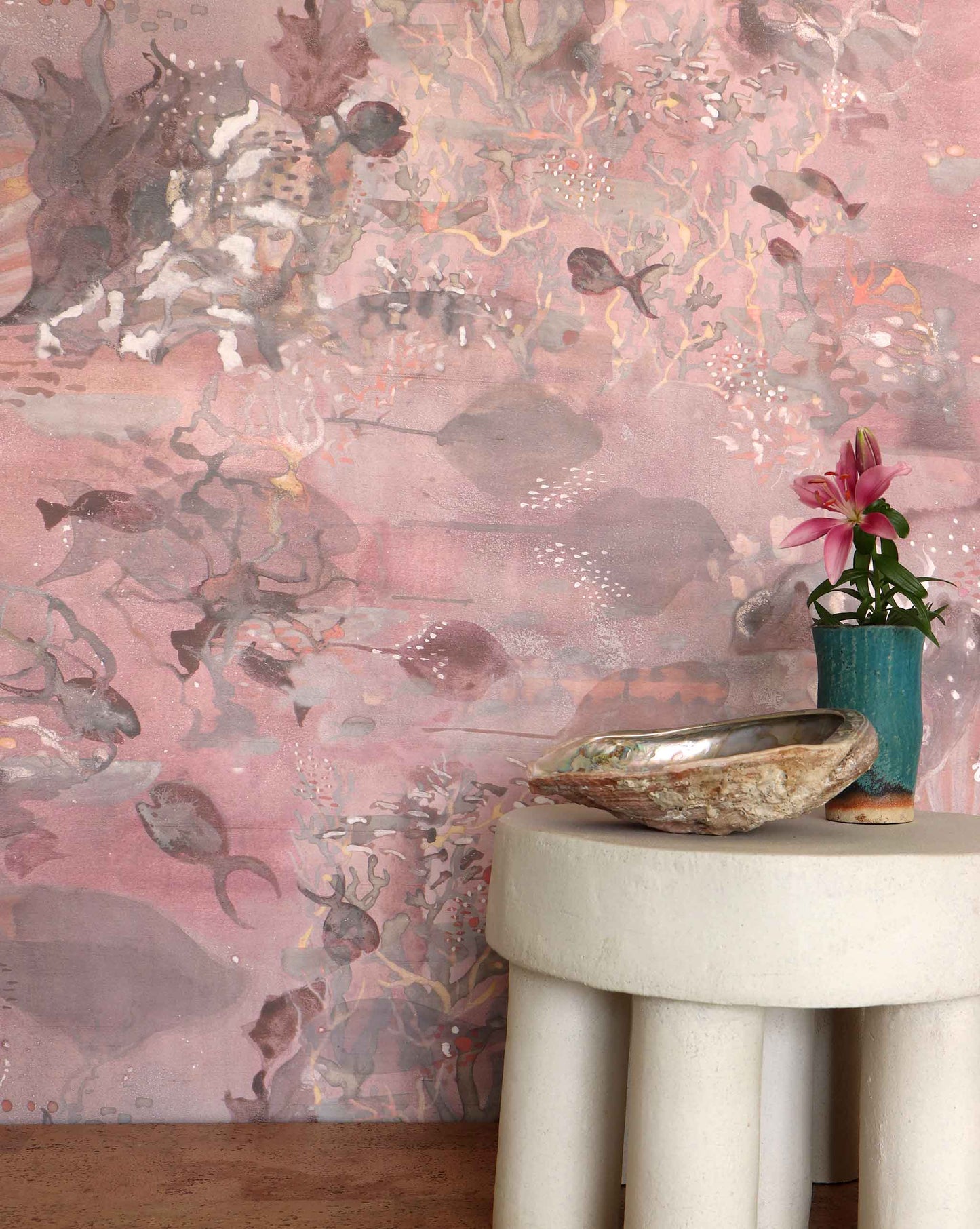 Eskayel’s Atoll wallpaper in Coral with its red hues is printed on a paper backed silk and installed in a room behind a stone stool.
