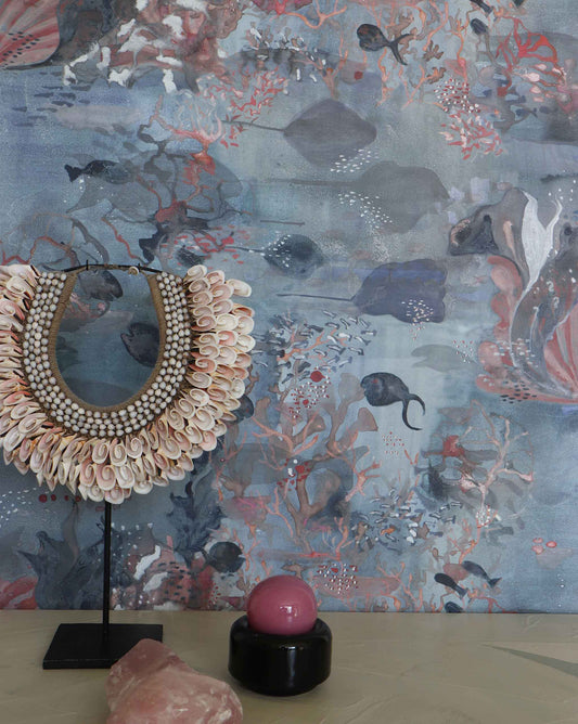 Eskayel’s Atoll wallpaper in Ocean with its blue hues is printed on a paper backed silk and installed in a room behind a shell necklace and table