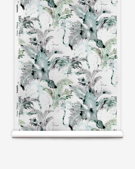 A roll of Cocos Silk Wallcovering||Chloros featuring a watercolor-style pattern with abstract leaves, palm tree motifs, and botanical shapes in shades of green, gray, and black.