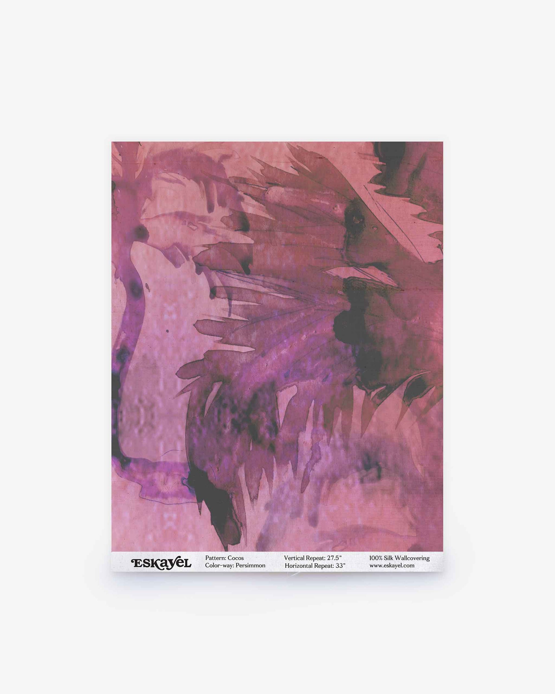 A square sample of the Cocos Silk wallpaper in the Persimmon colorway, showcasing abstract, watercolor-inspired patterns in shades of pink and purple, with product details printed along the bottom edge. Order a sample to experience its colors and texture firsthand.