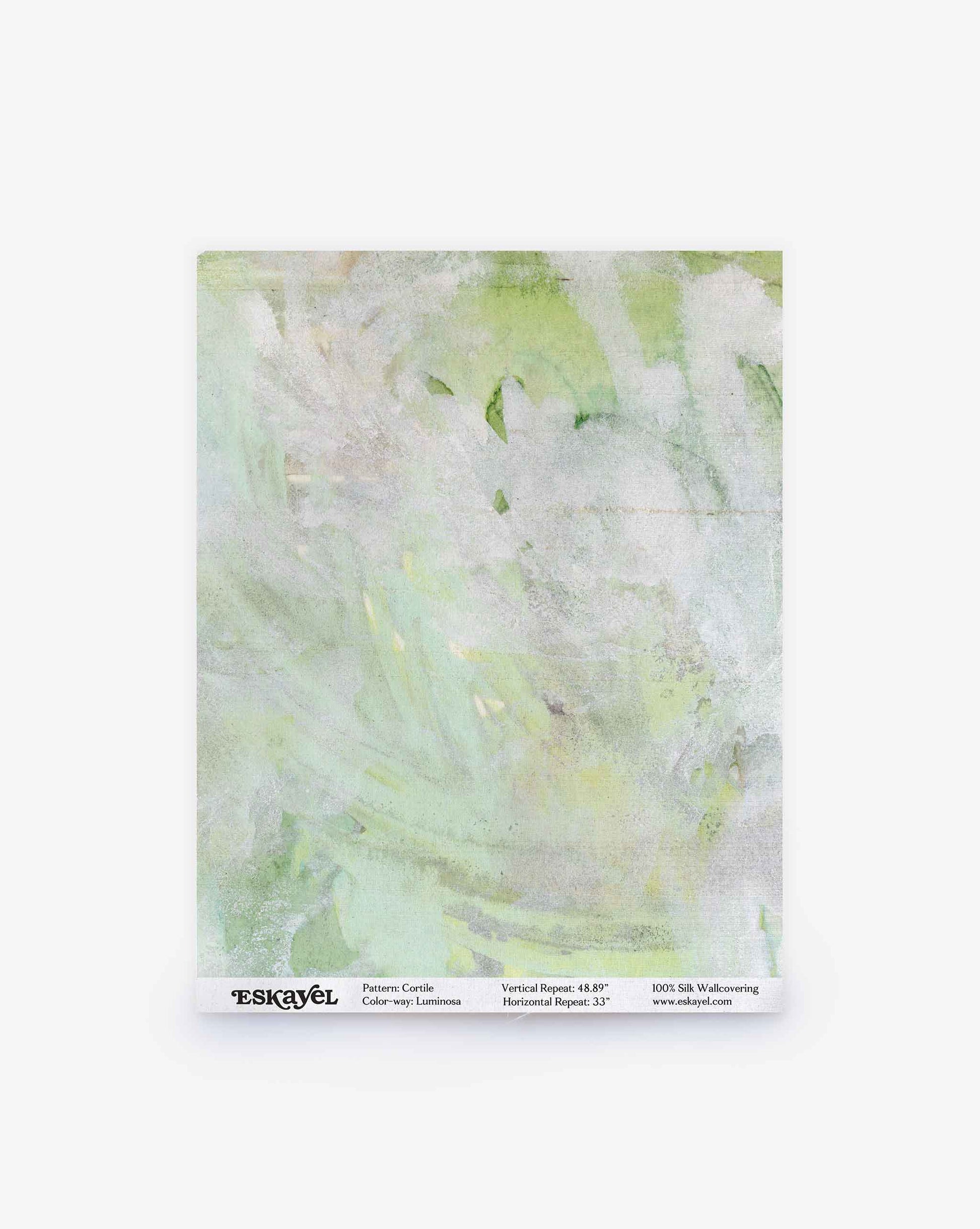 A sample of Cortile Silk Wallcovering||Luminosa featuring a light green and white abstract watercolor design, evocative of an Italianate garden, displayed on a square sheet with product information at the bottom.