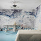 Bedroom with light beige bed, blue carpet, and an Empyrean Silk Mural||Air wallcovering featuring an abstract cloud theme. The room features a small table with a chair and a ceiling light fixture, creating an ethereal atmosphere.