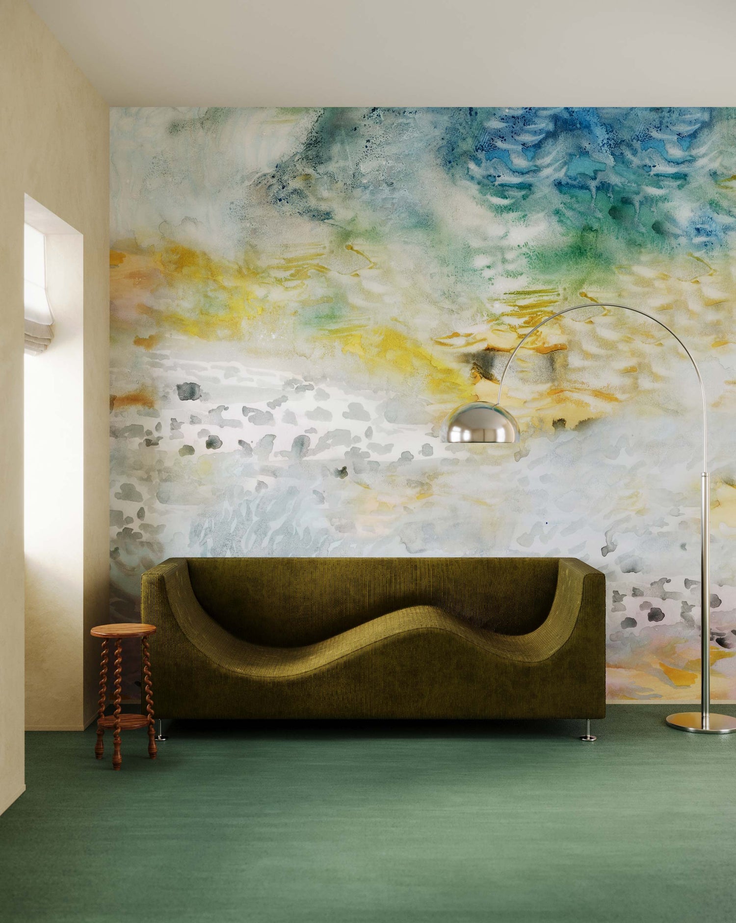 A modern living room features a green, curved sofa against an Empyrean Silk Mural in the Dawn design, echoing the serene hues of Maldivian sunsets. A metal floor lamp arches over the sofa, while a small wooden side table flanks the scene.