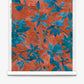 A roll of Plumeria Shadows Silk Wallcovering in the Hibiscus colorway, featuring a pattern of blue leafy branches set against a rich red-orange background.