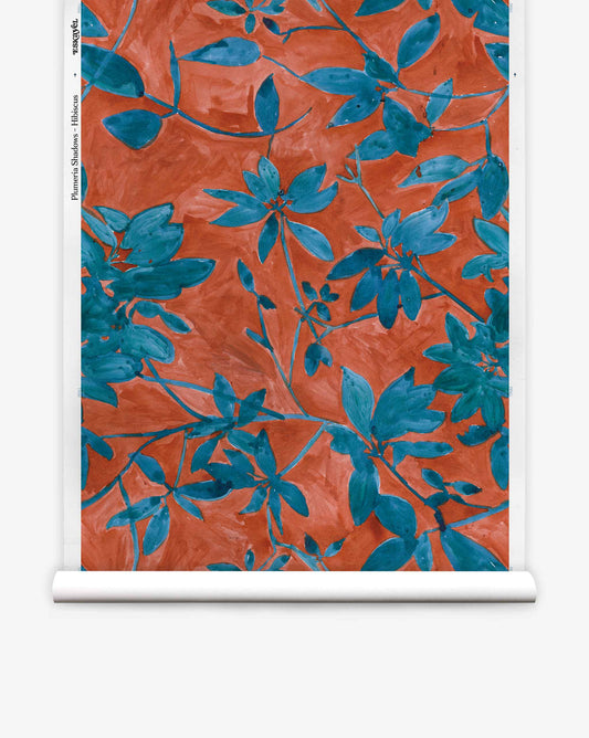 A roll of Plumeria Shadows Silk Wallcovering in the Hibiscus colorway, featuring a pattern of blue leafy branches set against a rich red-orange background.