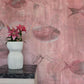 Eskayel’s Shoal wallpaper in Coral with its red hues is printed on paper backed silk and installed in a room behind a side table with a vase of flowers on top.