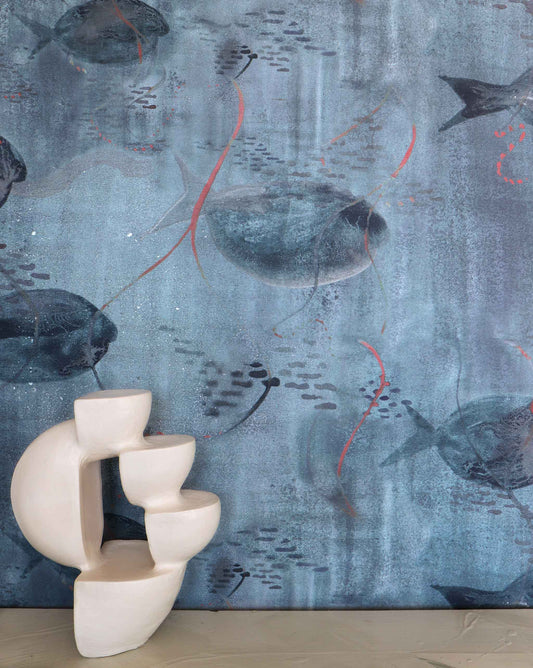 Eskayel’s Shoal wallpaper in Ocean with its blue hues is printed on paper backed silk and installed in a room behind a table with a stone sculpture on top.