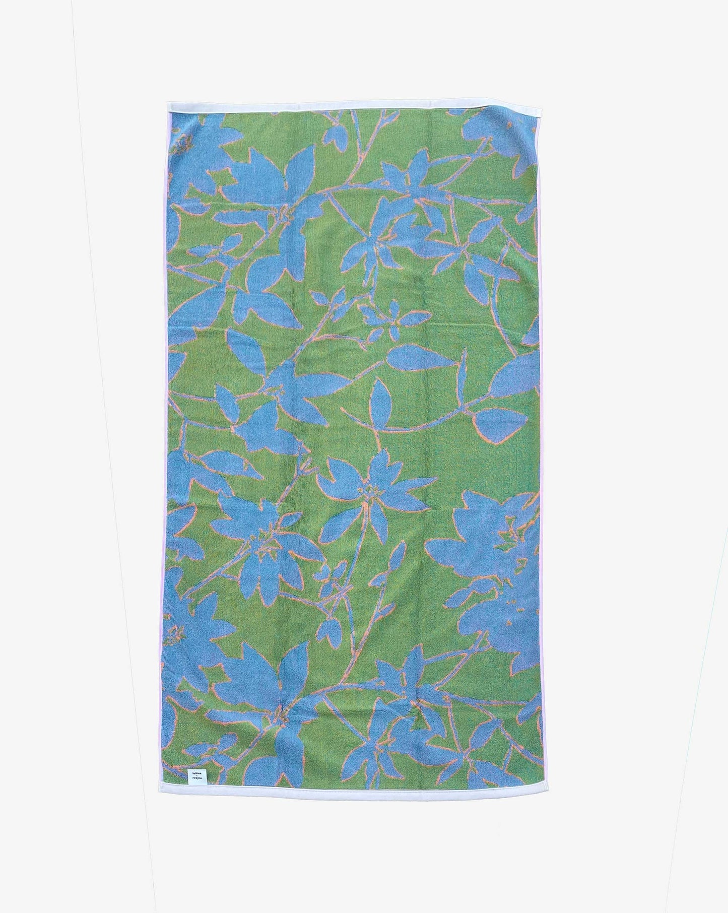 The reverse side of the Eskayel x Meleau Plumeria Shadows beach towel displays apple green, teal, and soft pink. 