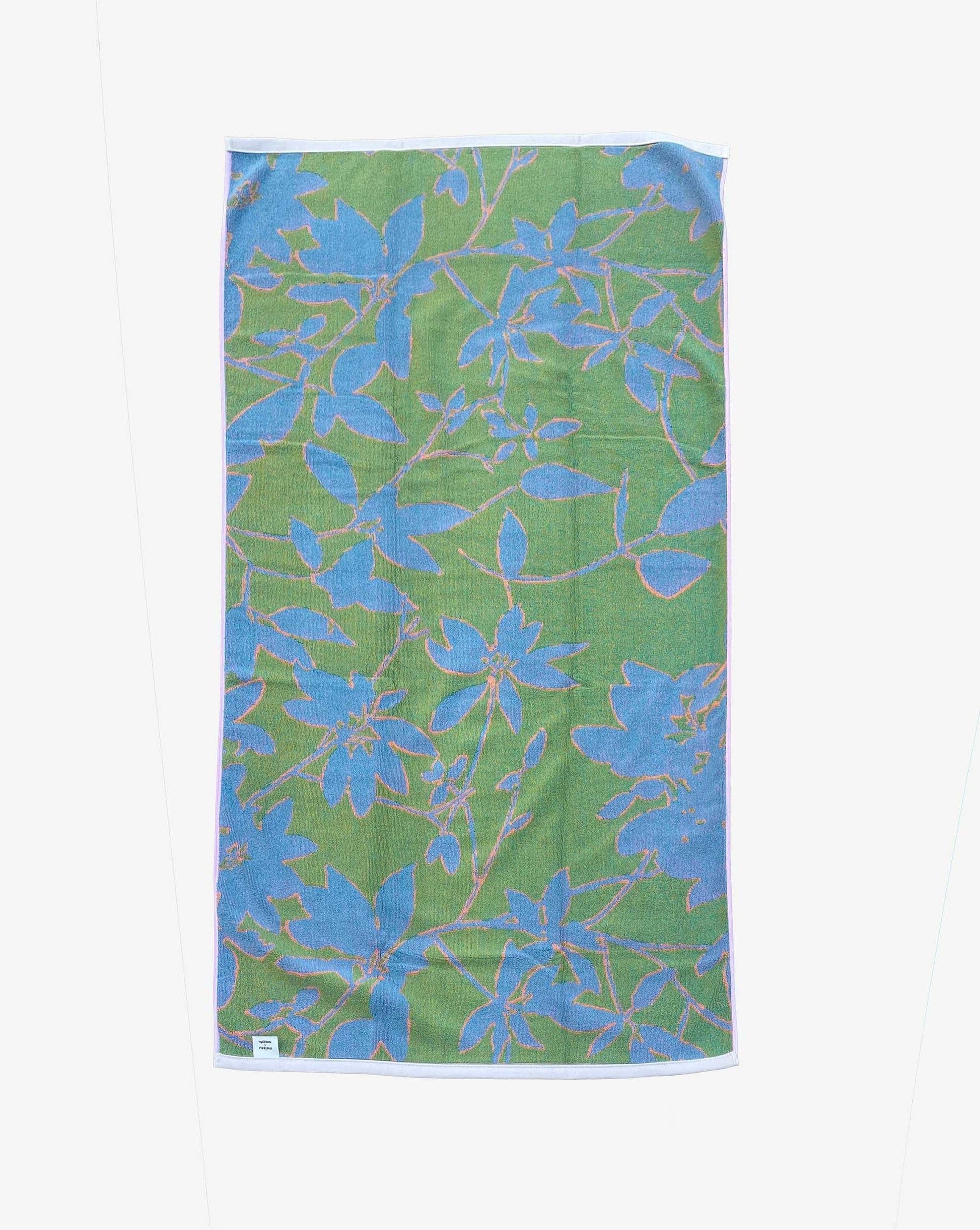 The reverse side of the Eskayel x Meleau Plumeria Shadows beach towel displays apple green, teal, and soft pink. 