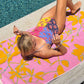 Eskayel's Founder Shanan Campanaro lounges by the pool on a Plumeria Towel, dressed in a colorful swimsuit.