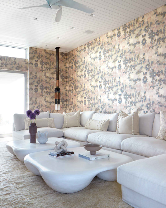 Modern living room with Clemente Wallpaper||Sol, a large white sectional sofa, unique white coffee tables, decorative books, and a hanging pendant light.