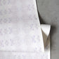 The Icelandic Mist Wallpaper in Lavender, featuring a subtle abstract pattern, lies rolled-up on a flat surface.