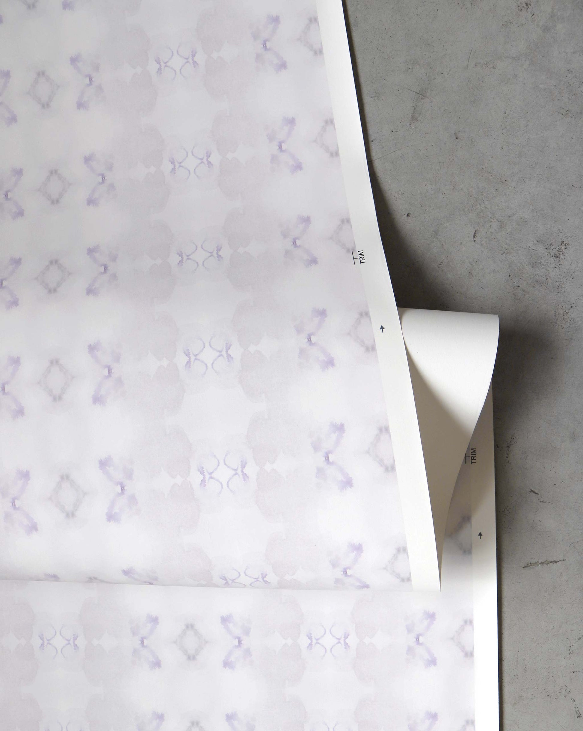 The Icelandic Mist Wallpaper in Lavender, featuring a subtle abstract pattern, lies rolled-up on a flat surface.