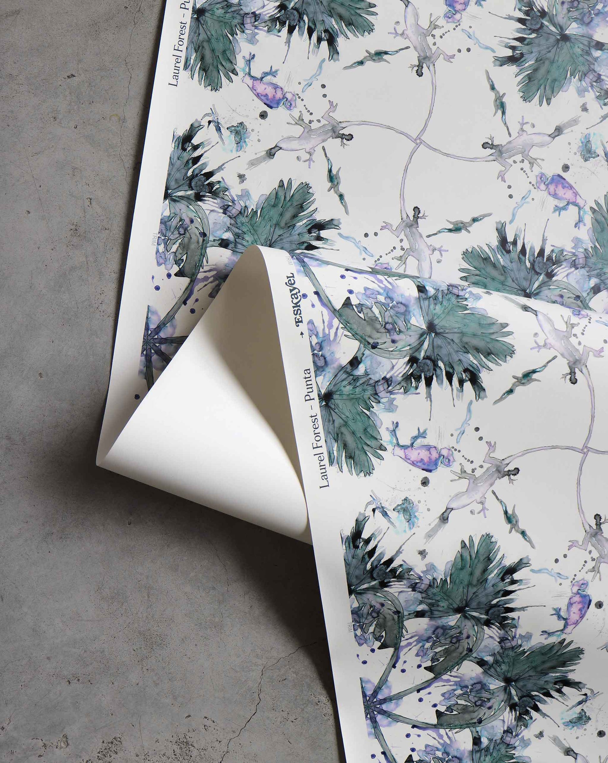 A close-up of a rolled-up Laurel Forest Wallpaper||Punta with a green and purple leafy design, partially unrolled on a gray surface, evokes the elegance of high-end wallpaper.