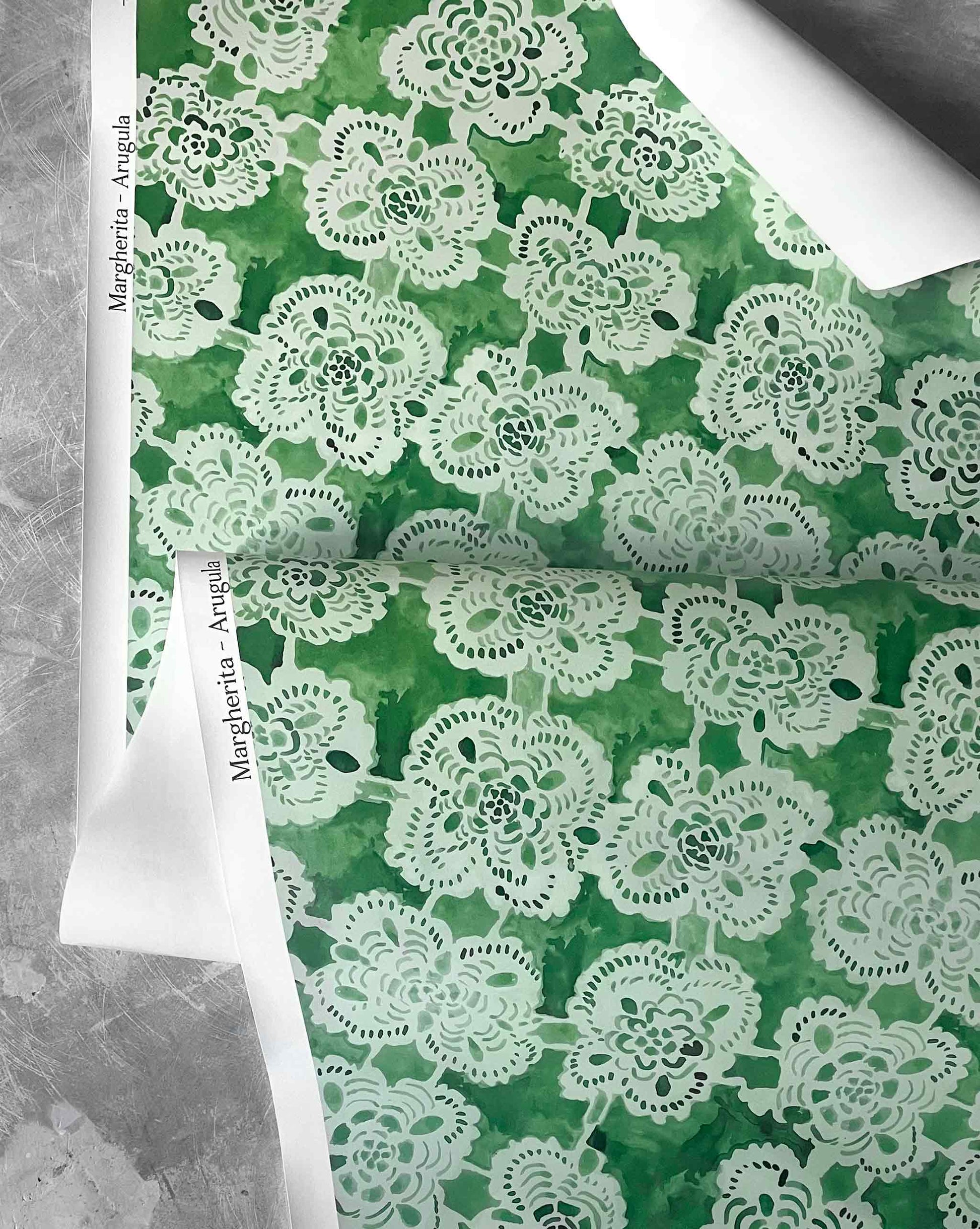 Green wallpaper with a white floral lace pattern on a gray surface.