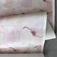A roll of Melting Checks Wallpaper with pink and white paint on it, offering color options for high-end Terracotta