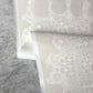 Close-up of a neutral lace wallpaper in Eskayel's Nonna's Lace Ricotta pattern on a textured gray surface.
