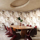 Shown installed on a dining room wall, Pétalos wallpaper by Eskayel in Solar is a warm colorway of earthy tones.