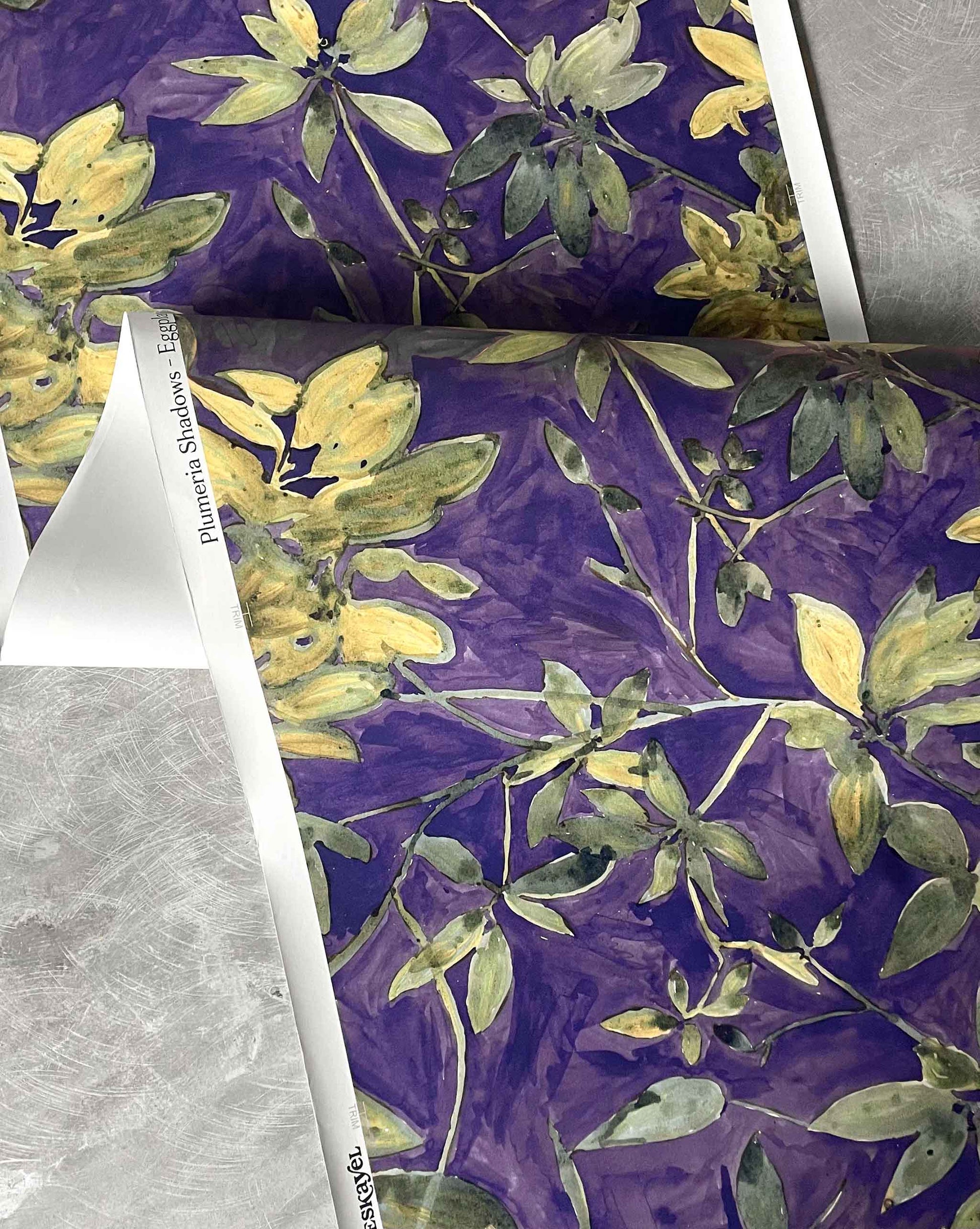 A detail photo of Eskayel’s Plumeria Shadows wallpaper pattern in Eggplant, a colorway of purple with green tones.