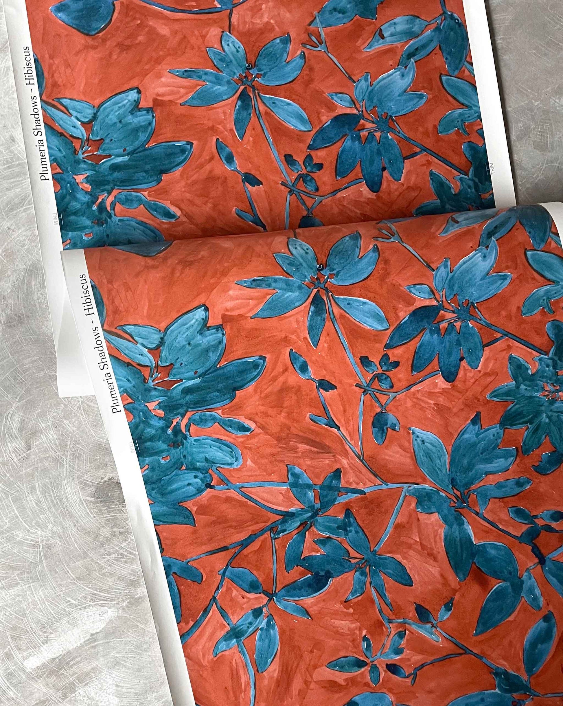 A detail wallpaper photo of Plumeria Shadows pattern in Hibiscus, a medium-sized repeat in the colorway featuring rich red background and gold tone leave | Eskayel