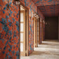 Plumeria Shadows Wallpaper Hibiscus — hand-painted tropical branches and leaves casting sharp shadows onto a stone patio in the midday sun form the basis of this pattern. Installed in a hallway in Hibiscus, a colorway of rich red and deep blue tones | Eskayel