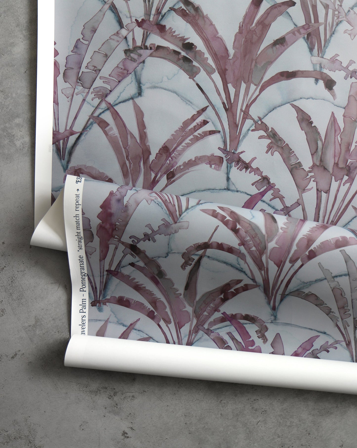 A roll of Travelers Palm Wallpaper Pomegranate with a geometric pattern and purple and blue leaves on it