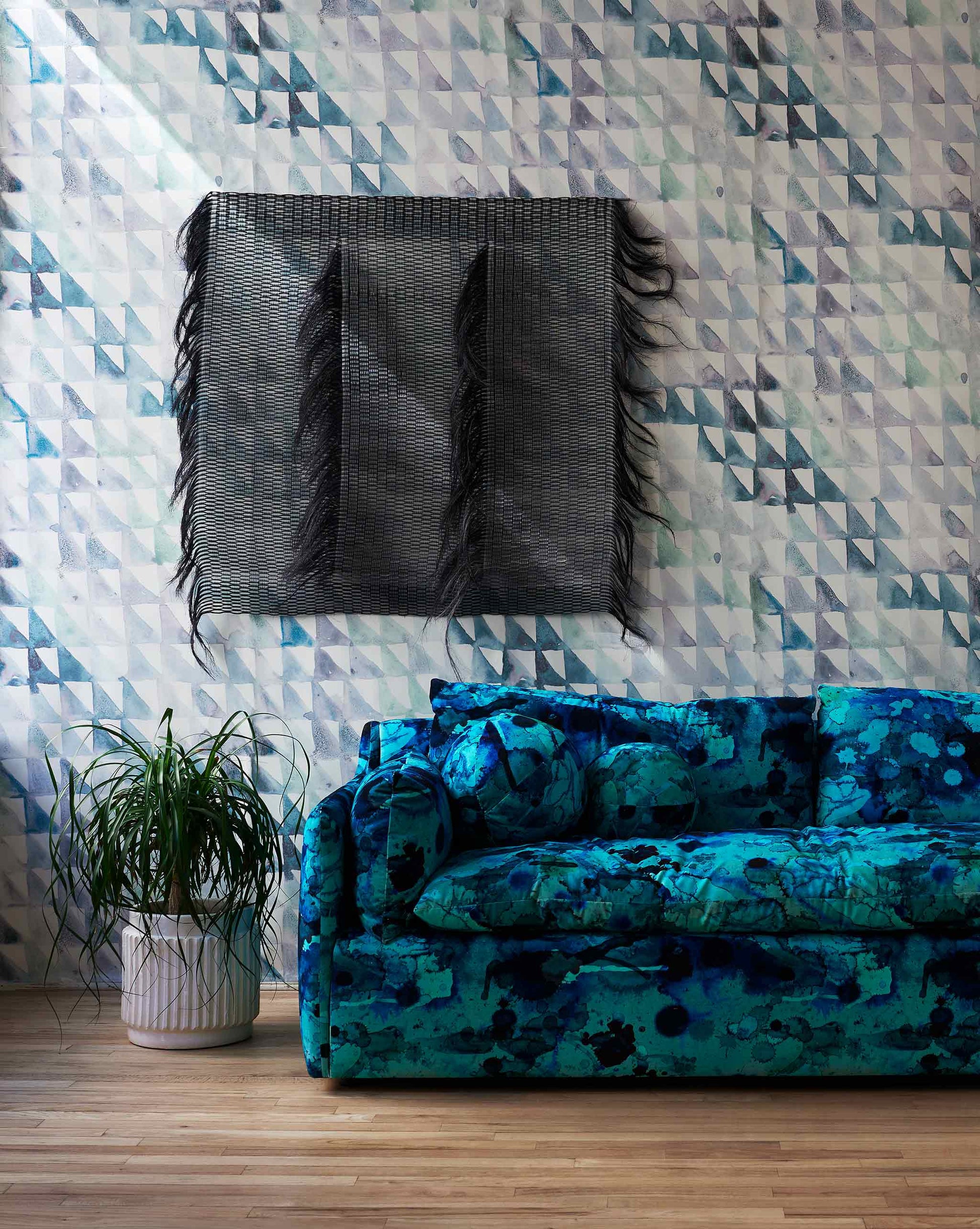 A blue sofa in front of a blue wall with Triangle Checks Wallpaper Verde design