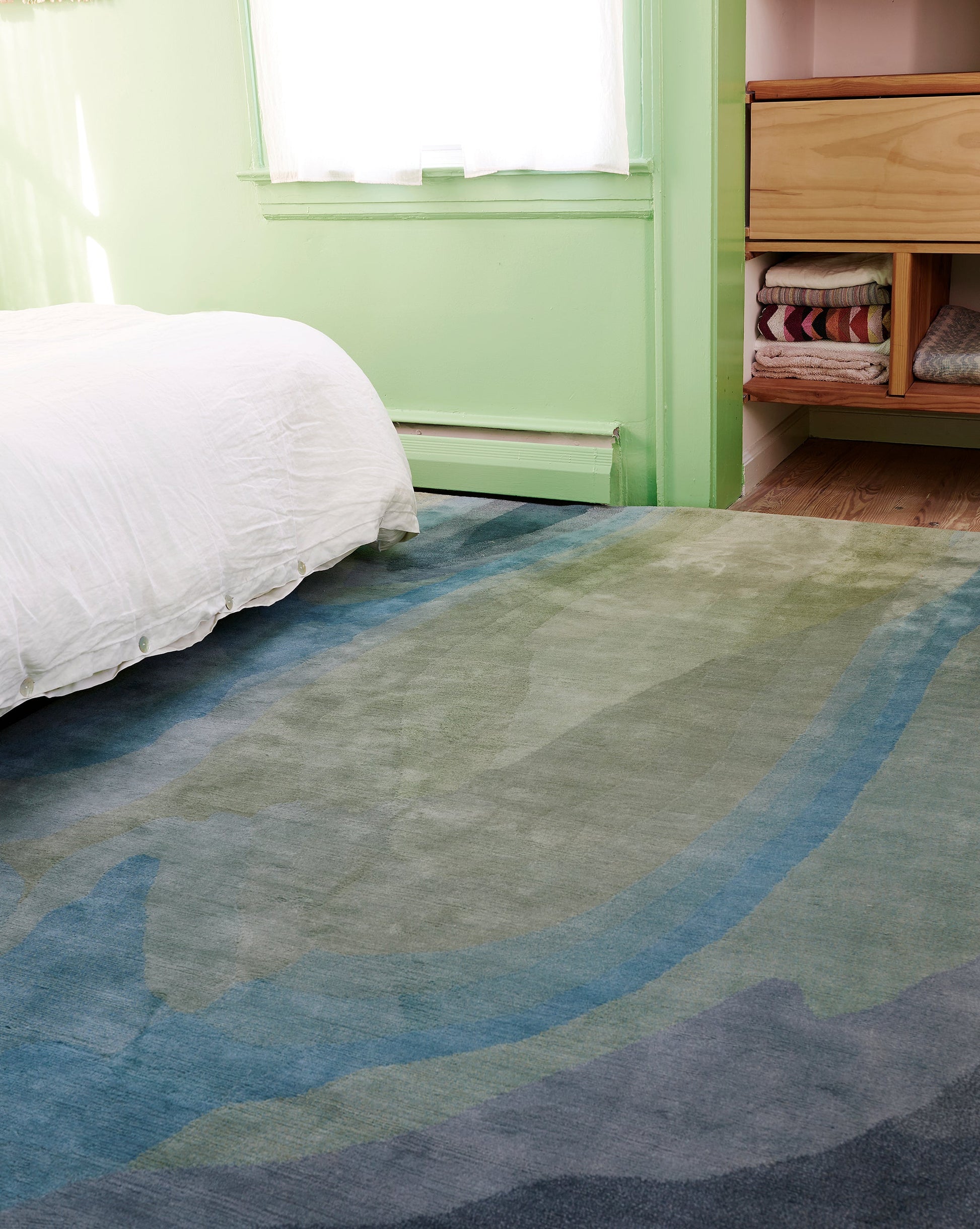 A green bedroom with a Progressions Hand Knotted Rug 5' x 8' in the Thalassa colorway.