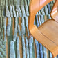 A curved wooden chair sits on our studio-designed Pyrus Stripe Hand Knotted Rug in Low Tide, which features textured, raised vertical blue and green stripes | Eskayel